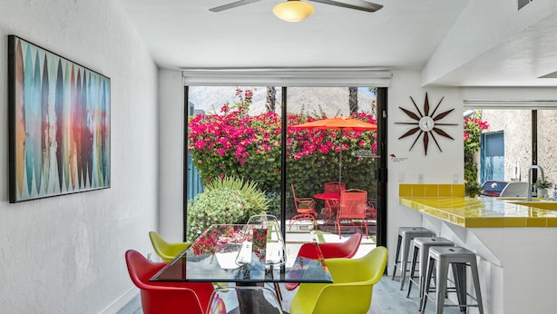 Una cocina moderna con una mesa de vidrio, sillas coloridas y un amplio ventanal con vistas a flores rosadas.