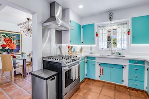 A modern kitchen with teal cabinets, a stainless steel stove, and a window with a view of the outdoors.