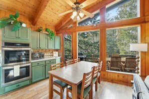 A wooden interior with a dining table, chairs, and a kitchen area with green cabinets and appliances.