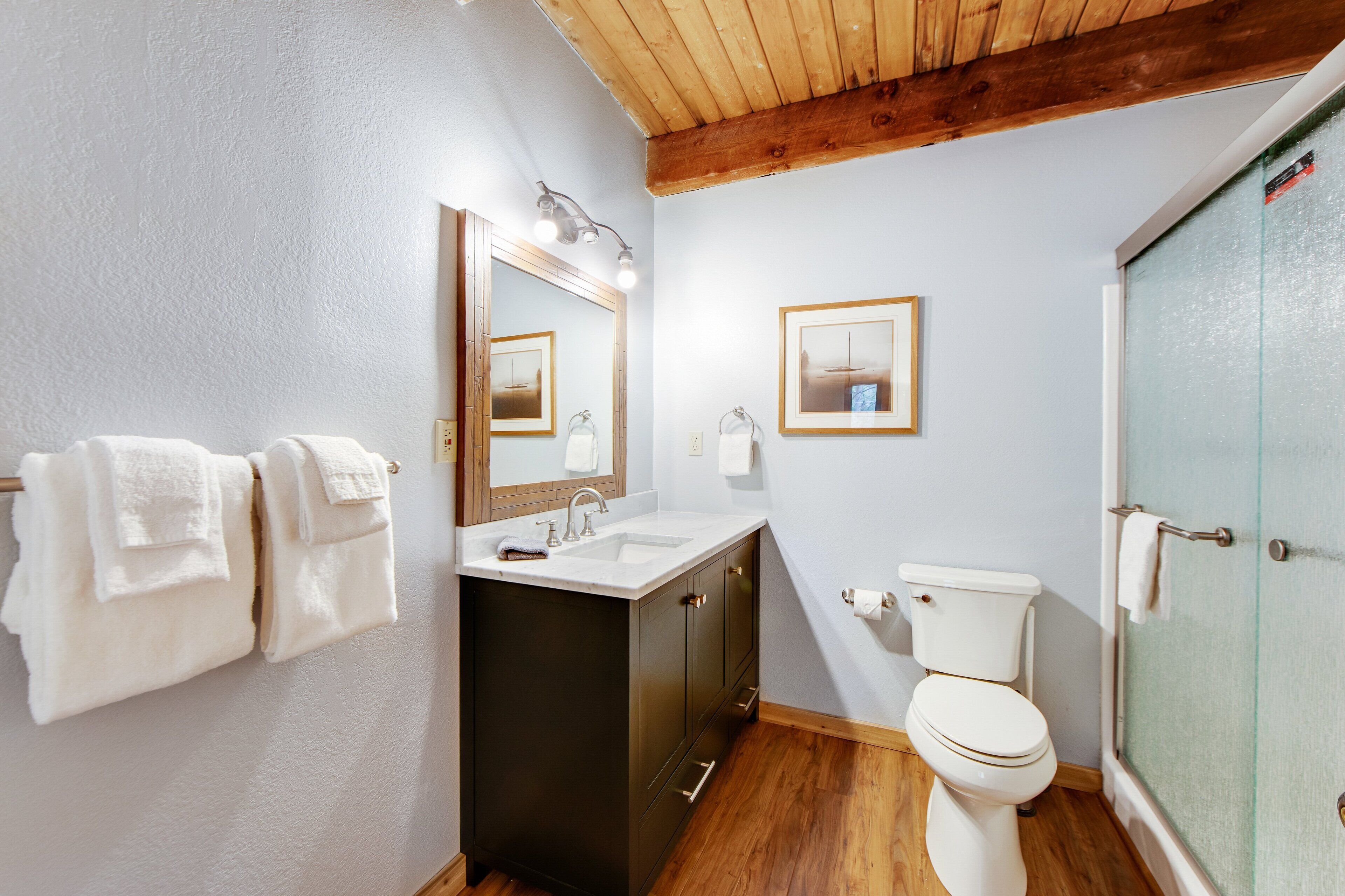 A bathroom with a wooden ceiling, a sink with a mirror, a toilet, and a glass shower door.