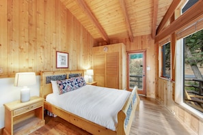 A wooden cabin bedroom with a bed, nightstands, and a window with a view of the outdoors.
