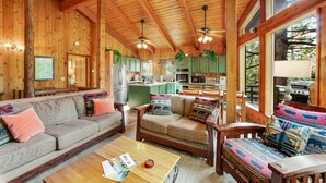 A cozy cabin interior with wooden walls, a sofa, a coffee table, and a kitchen area.