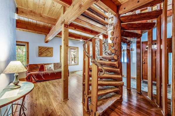 A wooden spiral staircase in a room with a wooden floor, a sofa, and a lamp.