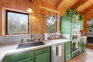 A kitchen with green cabinets, a stainless steel sink, and a hanging pot rack.