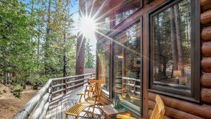 A wooden deck with chairs and a table, overlooking a forested area.