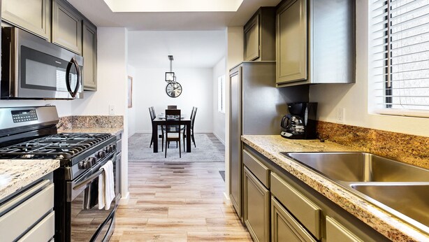 Una cocina moderna con encimeras de granito, electrodomésticos de acero inoxidable y un comedor con mesa y sillas.