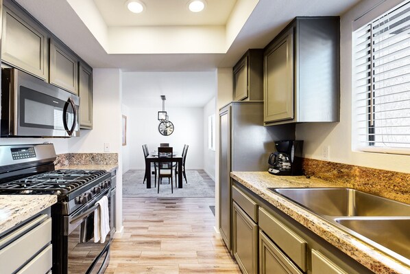 A modern kitchen with granite countertops, stainless steel appliances, and a dining area with a table and chairs. - Dual-Suite Canyon Country Club Estados Condo | Pool, Hot Tub & Tennis (Palm Springs)