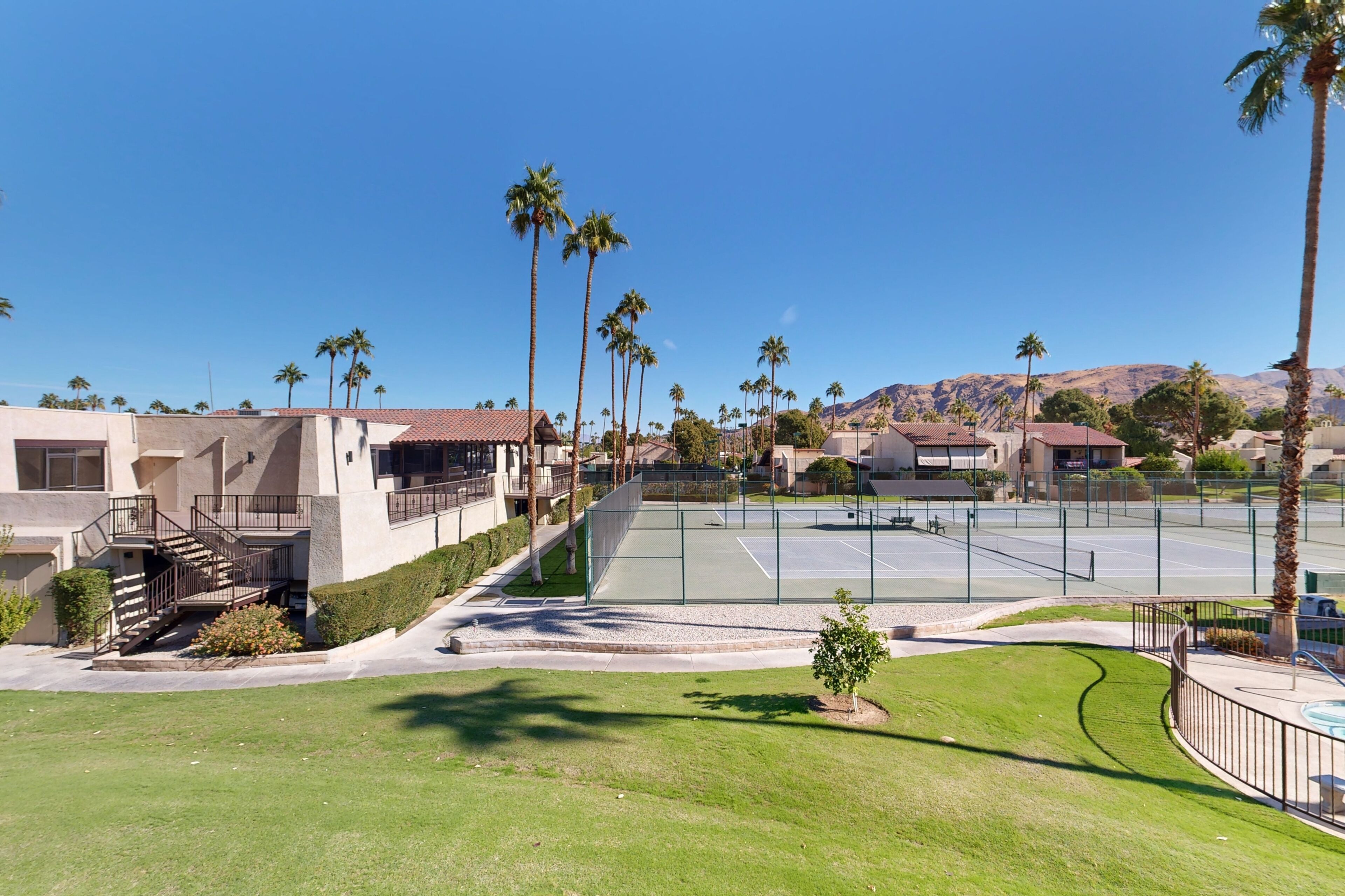 A residential area with a tennis court, palm trees, and houses with a hilly backdrop.