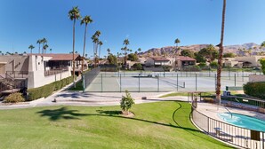 Zona residencial con cancha de tenis, palmeras y casas al pie de una montaña.
