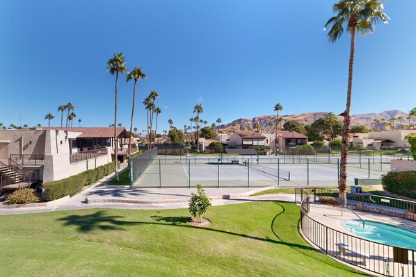 Zona residencial amb una pista de tenis, palmeres i cases amb muntanyes al fons.