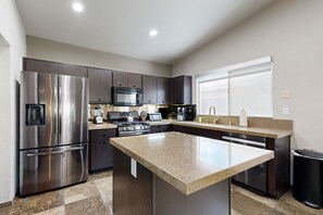 A modern kitchen with stainless steel appliances, dark cabinetry, and a granite countertop island. - Luxe La Quinta Haven with Private Pool, Spa & Pool Table 4BR #067085 (La Quinta)