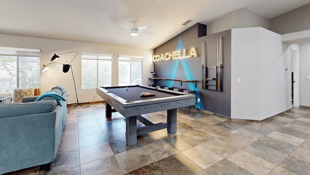 A modern living room with a pool table, a sofa, and a neon sign reading "COACHELLA".