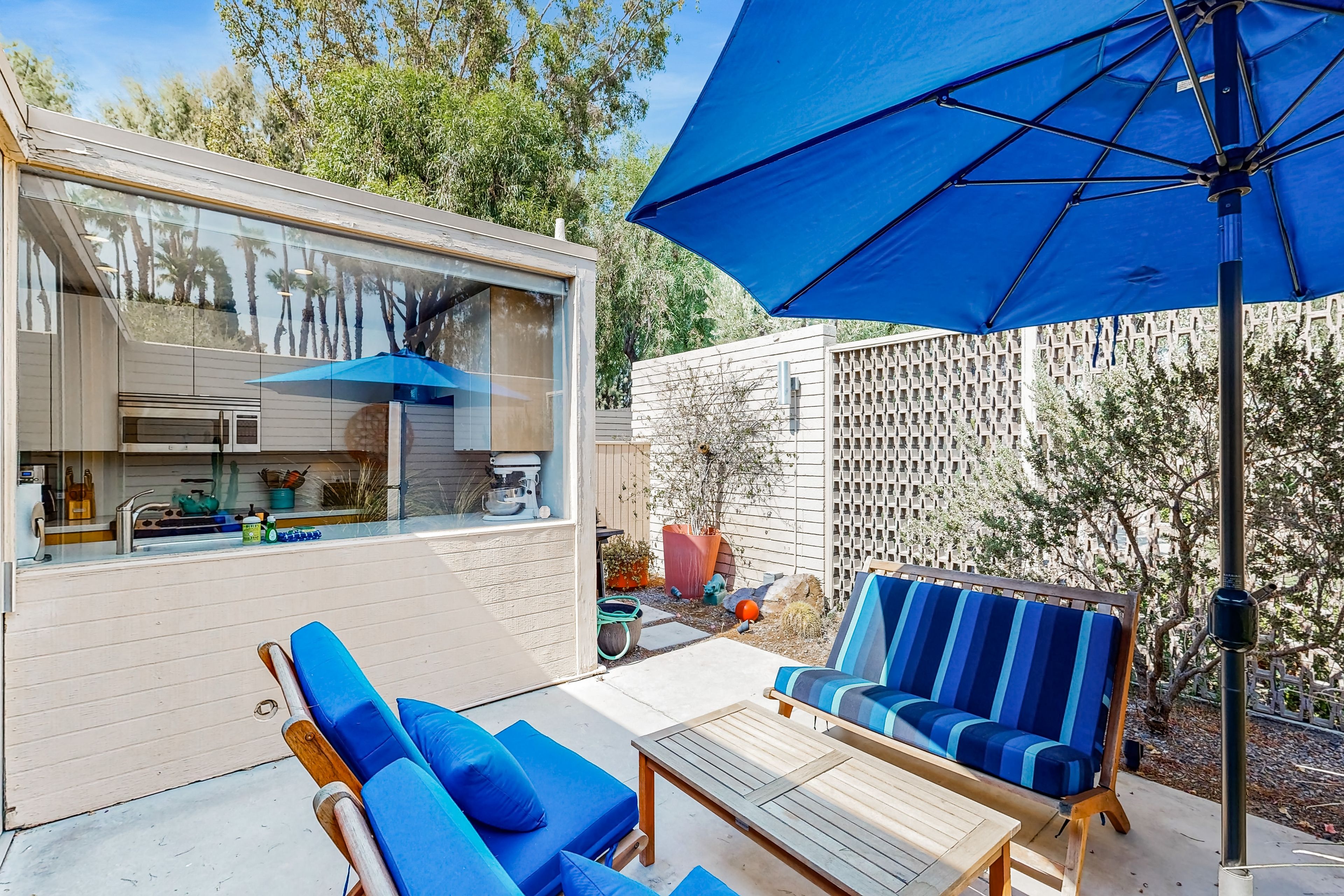 Une terrasse extérieure moderne, dotée d’une cuisine, de meubles bleus et d’un grand parasol.
