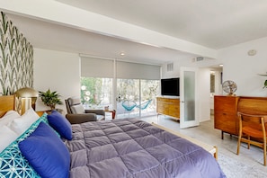 Une chambre moderne avec un grand lit, une télévision, une commode en bois et un balcon donnant sur la forêt.