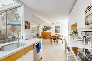 Une cuisine moderne dotée d’un îlot central, d’un coin repas avec des chaises et offrant une vue sur l’extérieur grâce à une grande fenêtre.