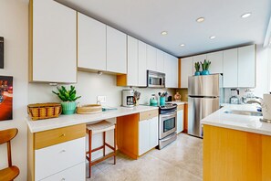 A modern kitchen with white cabinets, stainless steel appliances, and a central island with seating. - Updated Mid-Century Gem | 3 Patios & Gas Grill | Near Downtown (Palm Springs)