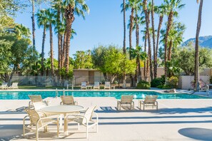 A pool area with lounge chairs and a table, surrounded by tall palm trees and a mountain in the background. - Updated Mid-Century Gem | 3 Patios & Gas Grill | Near Downtown (Palm Springs)