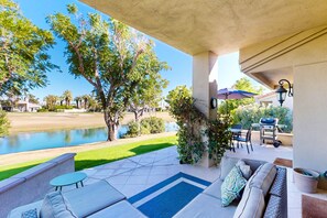 Un patio couvert avec coin salon extérieur, un barbecue et une vue sur un terrain de golf et un lac.