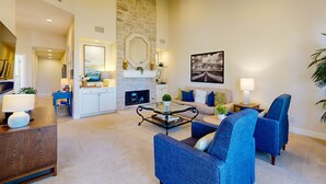 Een ruime woonkamer met een open haard, blauwe fauteuils, een bijzettafeltje en een groot schilderij aan de muur.