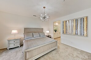 Ein Schlafzimmer mit einem großen Bett, Nachttischen, einer modernen Chandelierleuchtre und einem großen abstrakten Gemälde an der Wand.