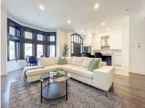 A modern living room with a sectional sofa, a glass coffee table, and a dining area with chairs. - Upscale Residence (Montréal)