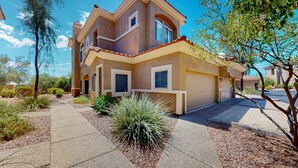 Une maison à deux étages avec un garage, une allée couverte et un jardin aménagé avec un petit arbuste.