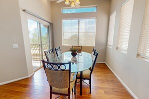 Un coin repas avec une table en verre, quatre chaises, une plante en pot et une vue sur l’extérieur grâce à de grandes fenêtres.