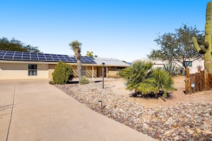 Una casa con paneles solares, un cactus y una pequeña palmera en el jardín.