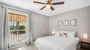 A bedroom with a bed, a ceiling fan, a nightstand with a lamp, and a window with curtains. - Dog-friendly sunshine stay with private pool, spacious yard, central AC & W/D (Tucson)