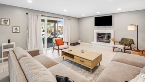 A modern living room with a sofa set, a coffee table, a fireplace, and a TV mounted on the wall. - Dog-friendly sunshine stay with private pool, spacious yard, central AC & W/D (Tucson)