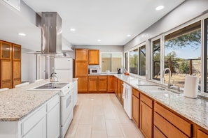 Cocina moderna con encimeras de granito, electrodom ésticos de acero inoxidable, armarios de madera y ventanas amplias con vistas al exterior.