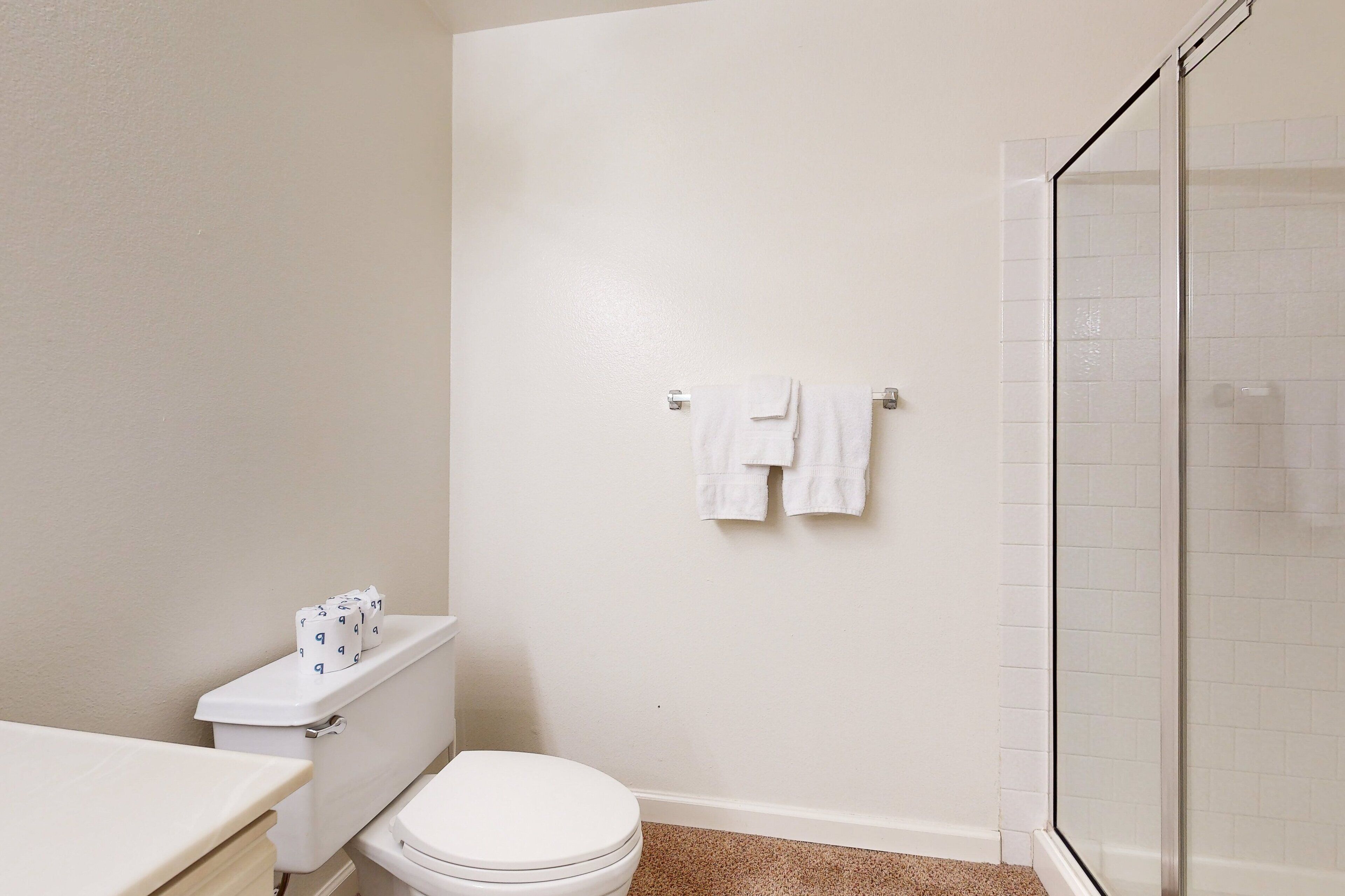 Et badeværelse med toilet, brusebad med glasdør og håndklæderække med to håndklæder.