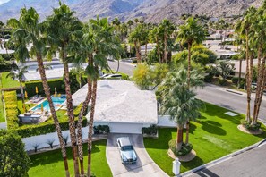 A residential property with a swimming pool, palm trees, and a car parked in the driveway. - Designer gem with private pool, spa, golf course & mountain views (Palm Springs)