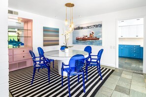 A modern dining area with a round table, blue chairs, and a black and white striped rug. - Designer gem with private pool, spa, golf course & mountain views (Palm Springs)