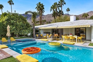 Zona de piscina con sillas amarillas y una mesa, rodeada de palmeras y una montaña al fondo.