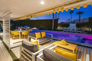 A poolside area with yellow and white furniture, a barbecue, and a view of palm trees and mountains. - Designer gem with private pool, spa, golf course & mountain views (Palm Springs)