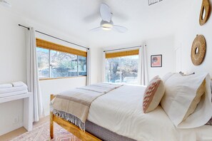 Ein Schlafzimmer mit einem Bett, einem Nachttisch, einem Deckenventilator und zwei Fenstern mit Jalousien.