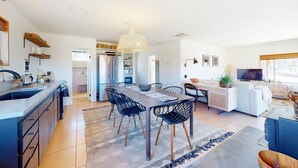 A modern kitchen with a central island, a dining area with a large table and chairs, and a living area with a sofa and TV. - Secluded hilltop home with hot tub, cowboy pool, & amazing views (Yucca Valley)