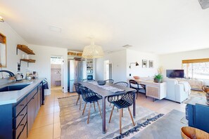 Eine moderne Küche mit Kochinsel, ein Essbereich mit großem Tisch und Stühlen sowie ein Wohnbereich mit Sofa und Fernseher.