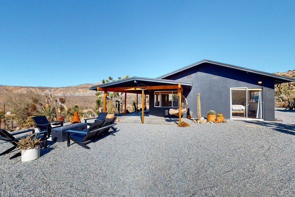 Ein modernes Haus mit einer überdachten Terrasse, Sitzgelegenheiten im Freien und Wüstenbepflanzung.