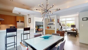 A modern kitchen with a central island, a dining area with a glass-top table, and a contemporary chandelier. - Mid-Century Jack LaLanne home with pool, spa & firepit (Palm Springs)