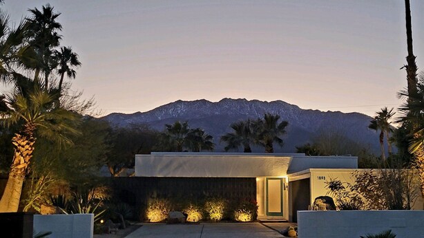 A modern house with a mountain backdrop, a well-lit entrance, and a minimalist design. - Mid-Century Jack LaLanne home with pool, spa & firepit (Palm Springs)