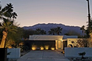 A modern house with a mountain backdrop, a well-lit entrance, and a minimalist design. - Mid-Century Jack LaLanne home with pool, spa & firepit (Palm Springs)