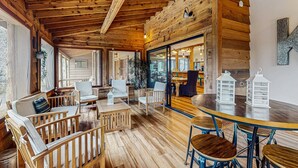 A cozy wooden interior with a dining area, seating, and a view through a glass door. - Stunning Fern Valley cabin with forest views & private hot tub - dog-friendly (Idyllwild)