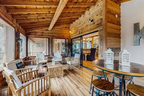 A cozy wooden interior with a dining area, seating, and a view through a glass door. - Stunning Fern Valley cabin with forest views & private hot tub - dog-friendly (Idyllwild)