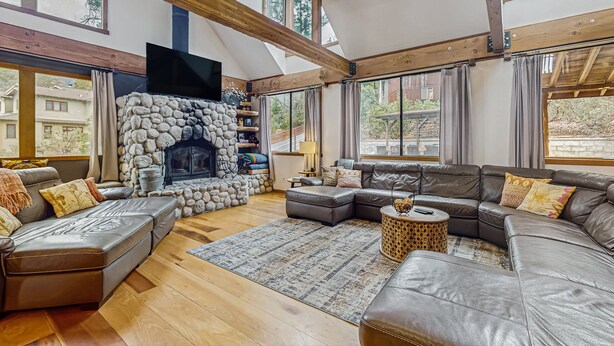 A spacious living room with a stone fireplace, leather sofas, and large windows. - Stunning Fern Valley cabin with forest views & private hot tub - dog-friendly (Idyllwild)