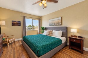 A hotel room with a bed, a desk, a chair, a nightstand, a lamp, a ceiling fan, and a window with curtains. - Welcoming condo with WiFi & pool - near Scottsdale Fashion Square (Scottsdale)