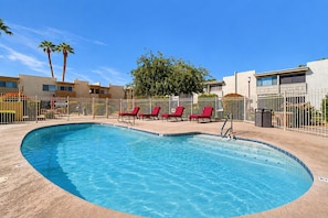 A swimming pool with red lounge chairs, surrounded by a fence, and palm trees in the background. - Welcoming condo with WiFi & pool - near Scottsdale Fashion Square (Scottsdale)