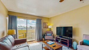 A modern living room with a sofa, coffee table, TV, and a balcony with curtains. - Welcoming condo with WiFi & pool - near Scottsdale Fashion Square (Scottsdale)