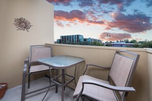 A balcony with two chairs and a table, overlooking a building with a sunset sky. - Welcoming condo with WiFi & pool - near Scottsdale Fashion Square (Scottsdale)